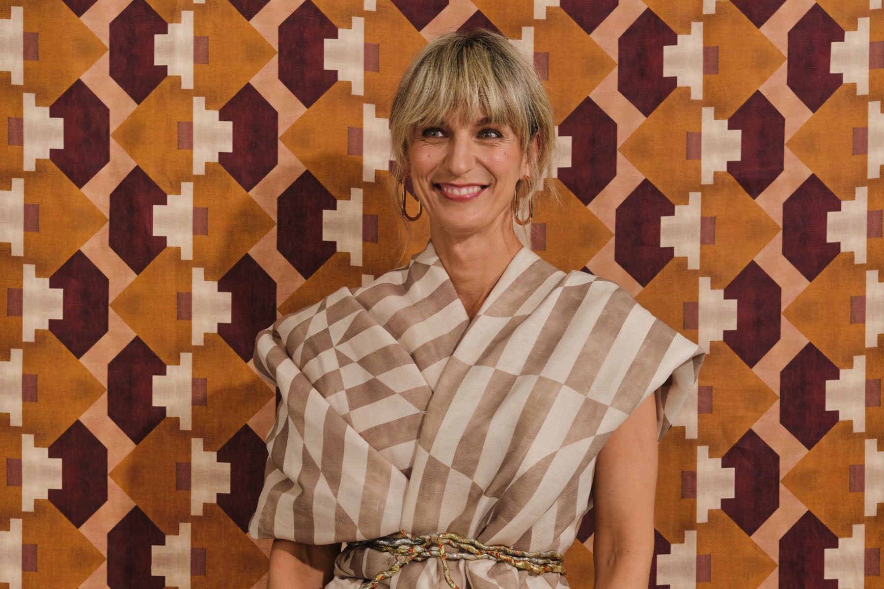 Portait of a blonde woman in a denim jumpsuit, against a colorful geometric background