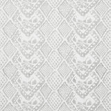Detail of wallpaper in a lacey diamond print in white on a gray field.