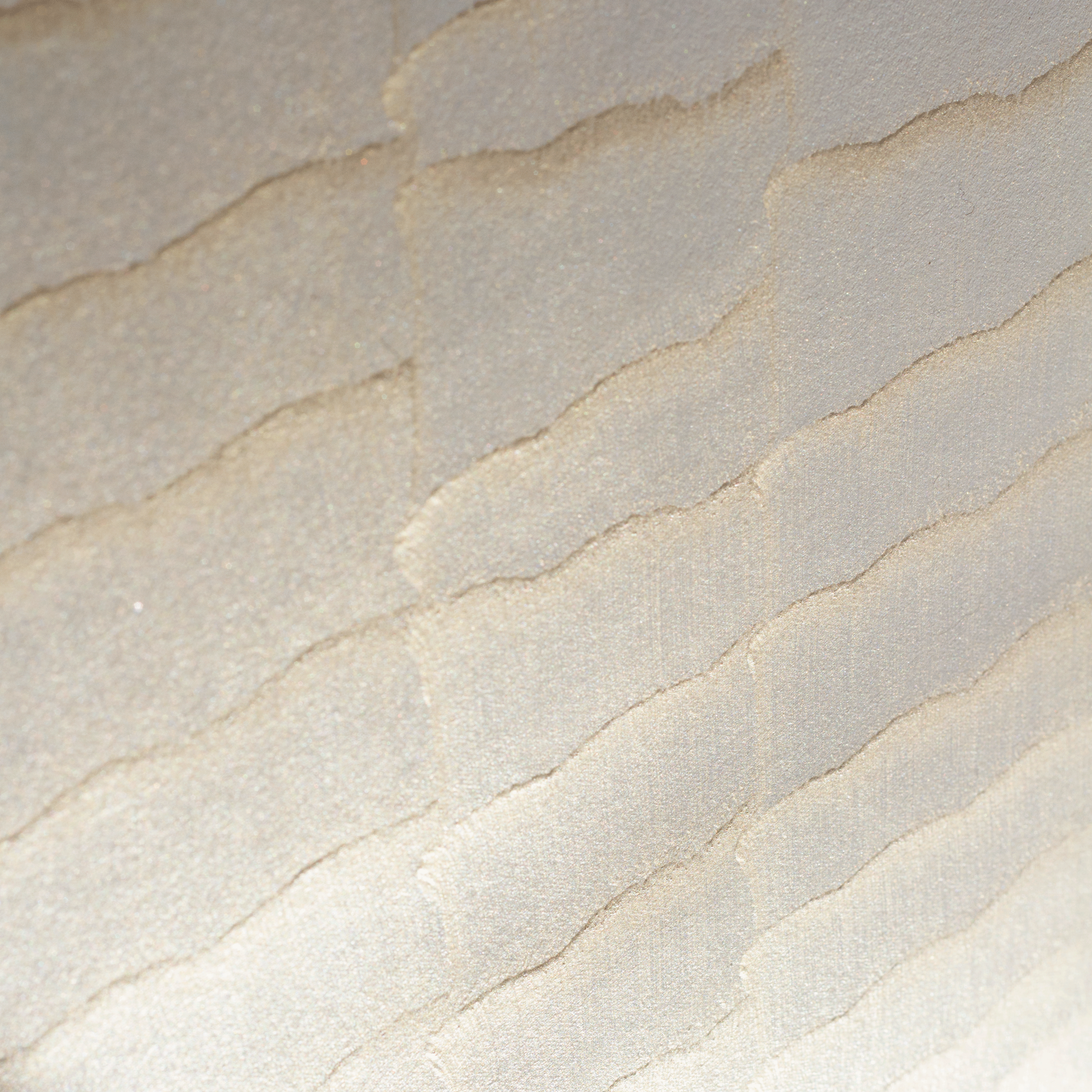 Wide-angle shot of wallpaper in an abstract textural pattern in metallic pink and cream.