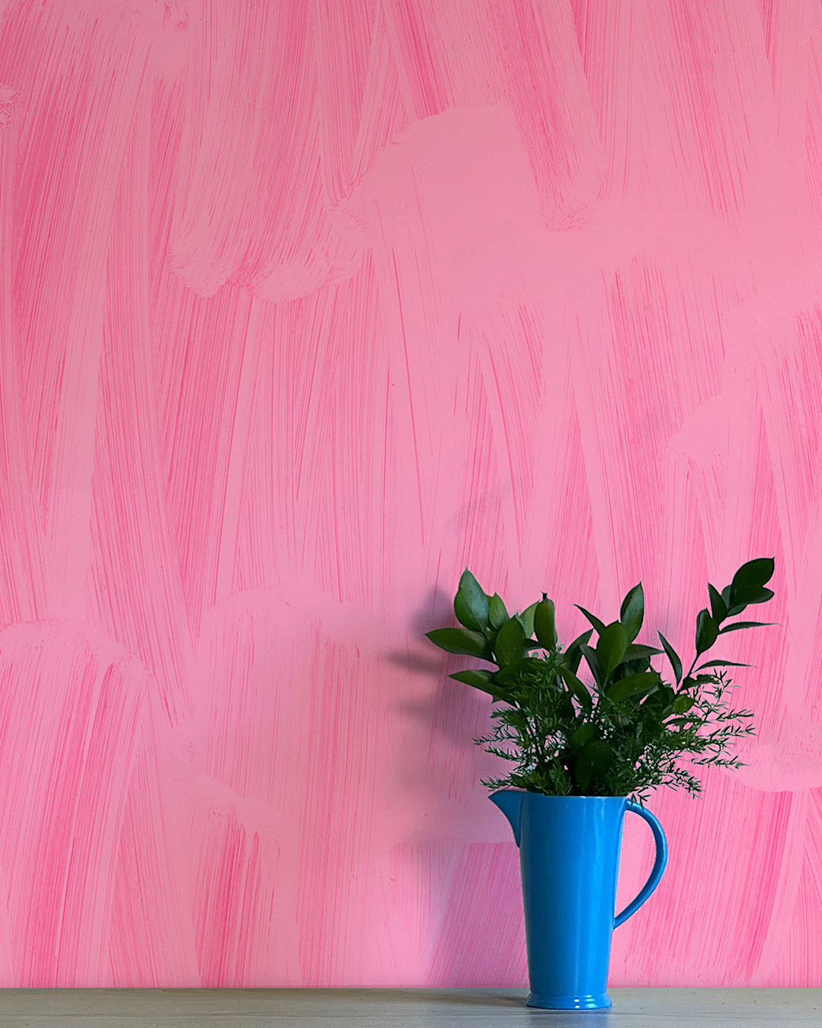 A vase of flowers stands in front of a wall papered in an abstract paint print in shades of pink.