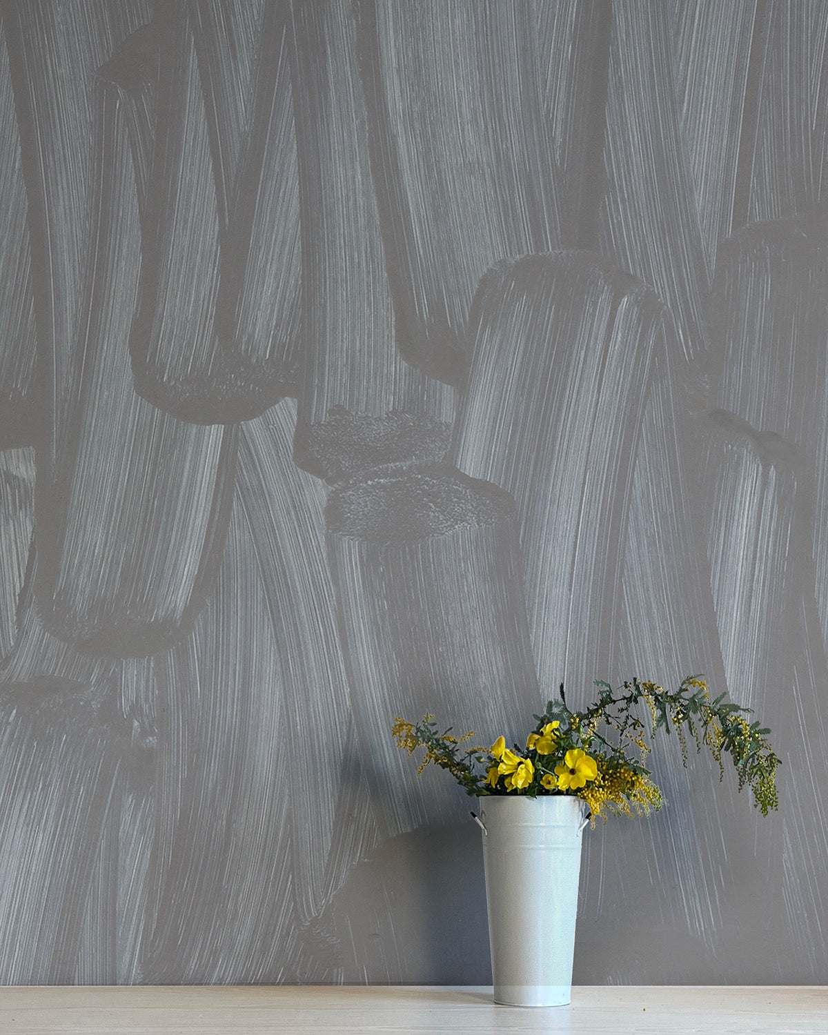A vase of flowers stands in front of a wall papered in an abstract paint print in shades of gray.