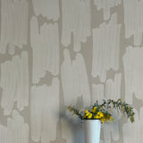 A vase of flowers stands in front of a wall papered in an abstract paint swatch print in light gray on a gray field.