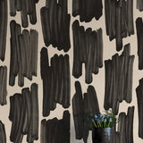 A vase of flowers stands in front of a wall papered in an abstract paint swatch print in black on a cream field.