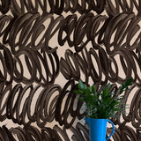 A vase of flowers stands in front of a wall papered in a playful paint print in black on a tan field.