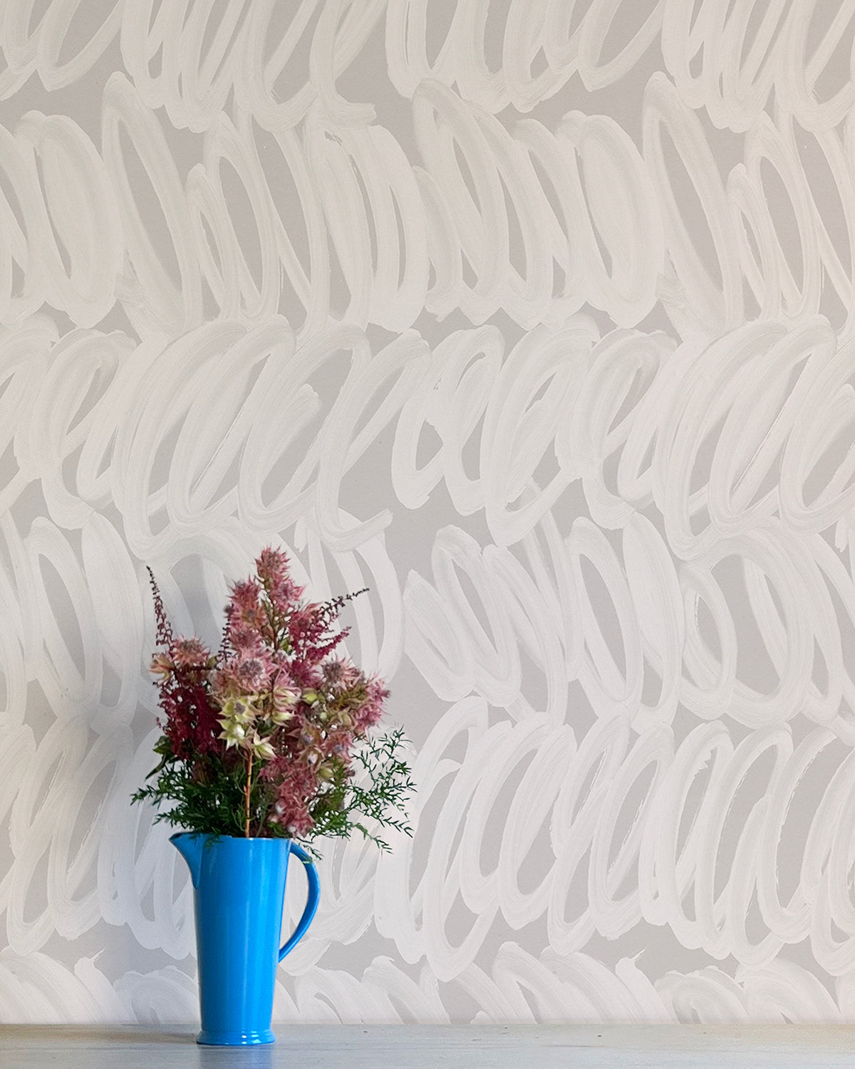 A vase of flowers stands in front of a wall papered in a playful paint print in cream on a gray field.