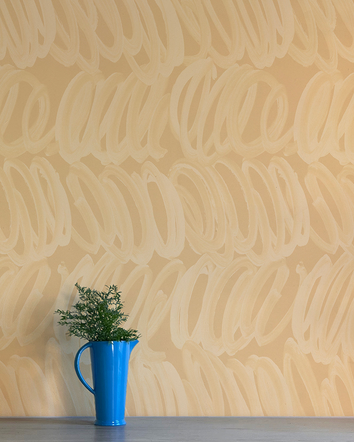 A vase of flowers stands in front of a wall papered in a playful paint print in cream on a tan field.