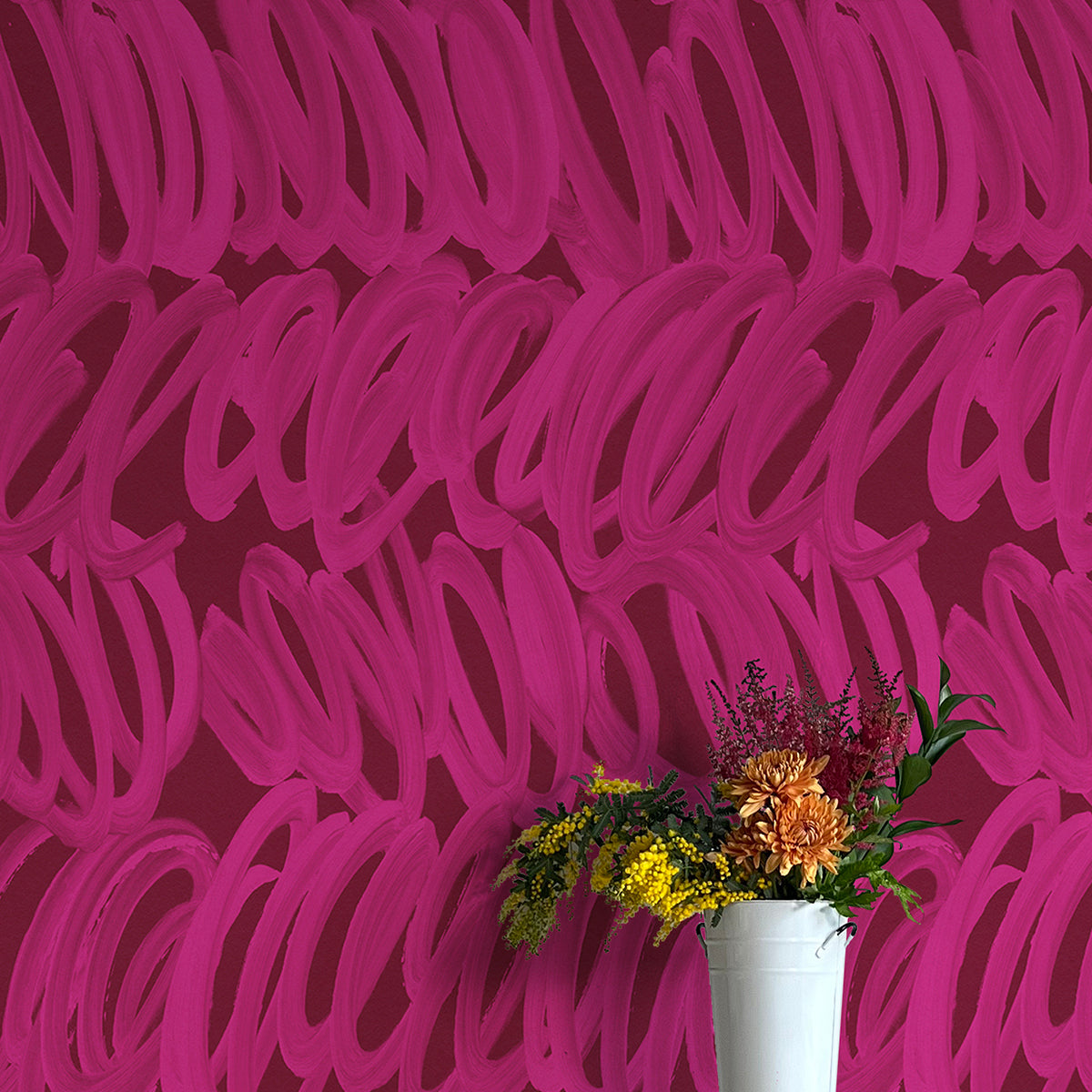 A vase of flowers stands in front of a wall papered in a playful paint print in pink on a maroon field.