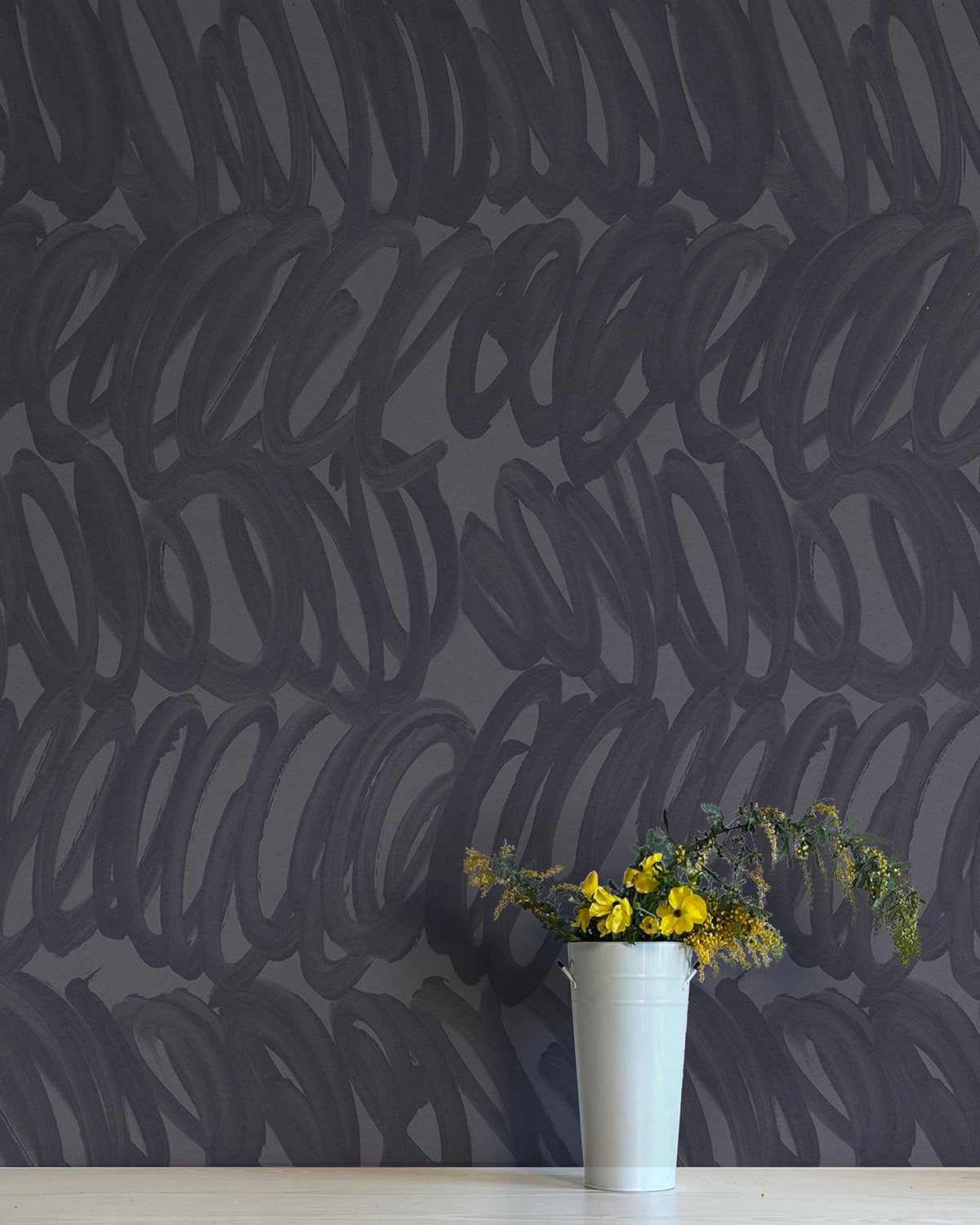 A vase of flowers stands in front of a wall papered in a playful paint print in charcoal on a gray field.