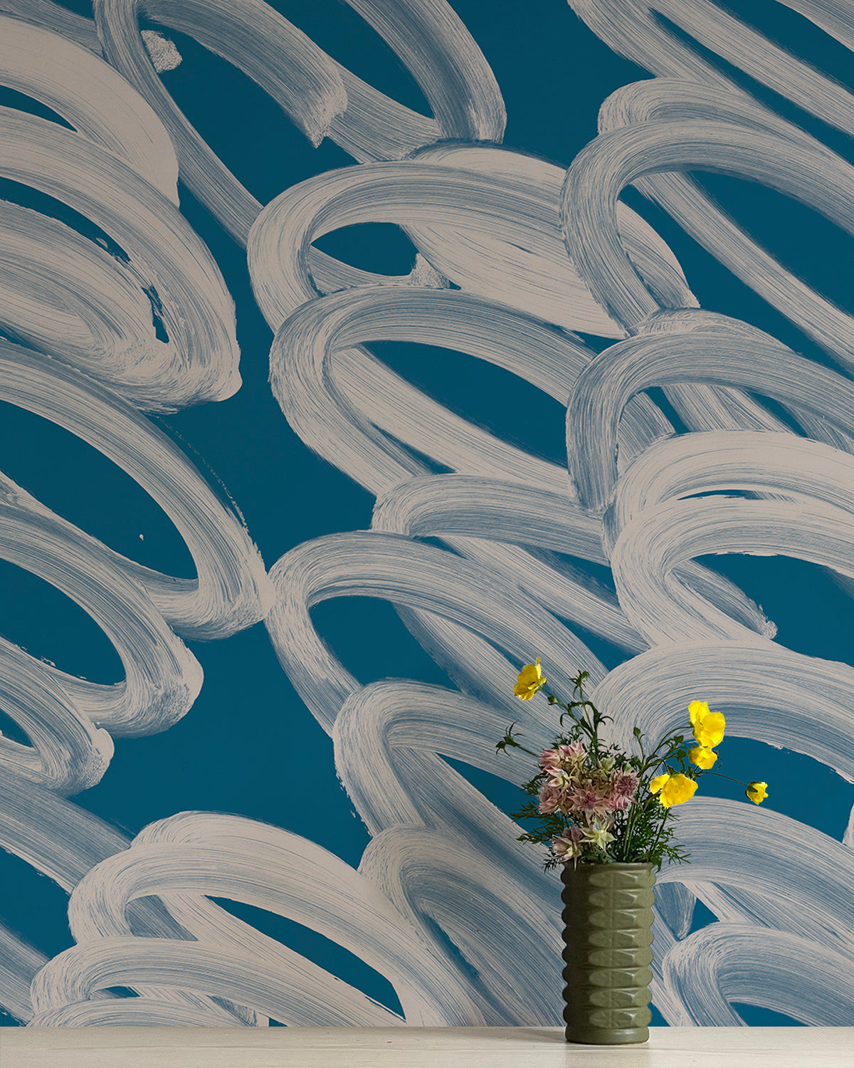 A vase of flowers stands in front of a wall covered in an abstract paintstroke print in cream on a navy field.