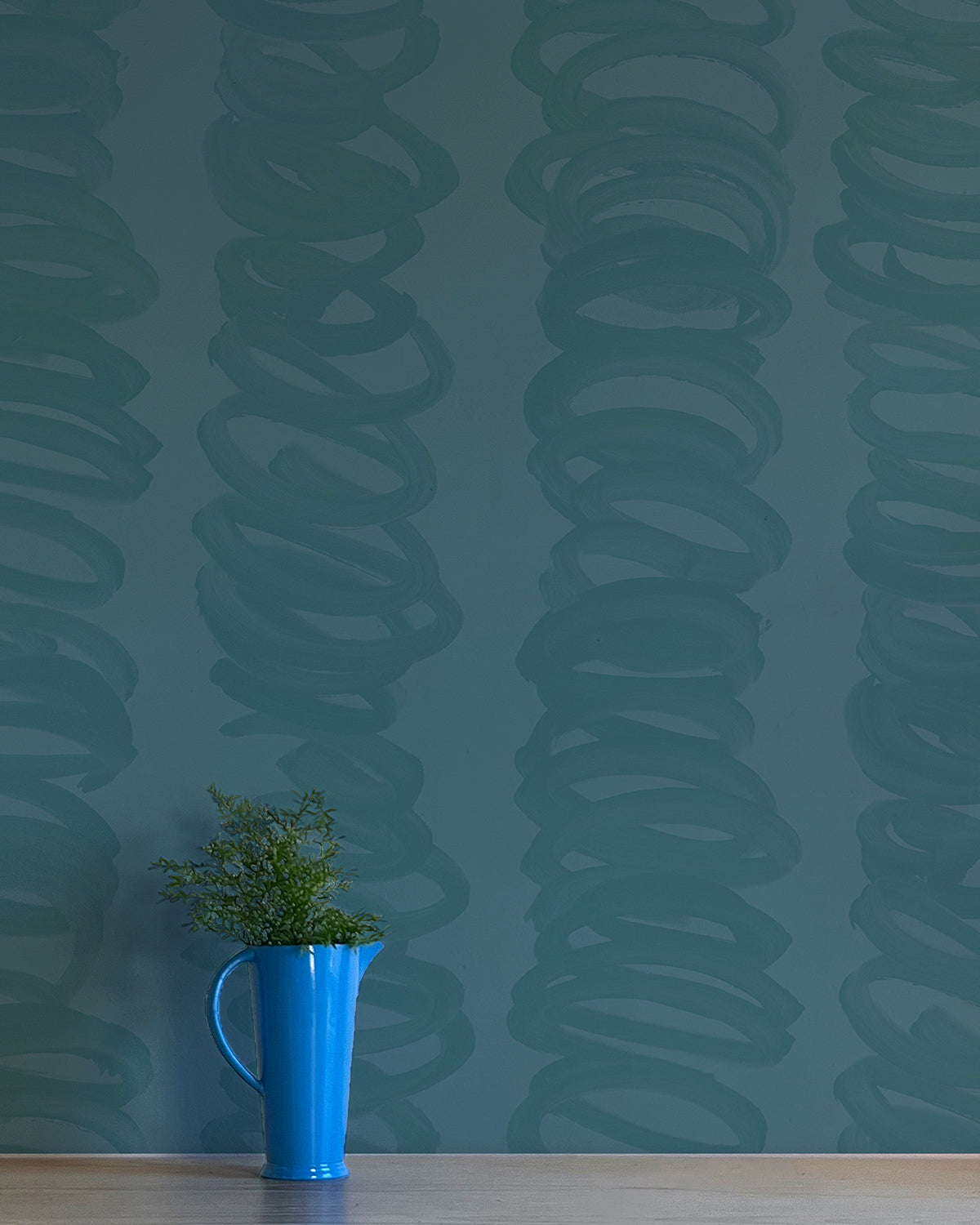 A vase of flowers stands in front of a wall covered in an abstract scribble print in navy on a turquoise field.