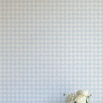 A vase of flowers stands in front of a wall papered in a dense plaid pattern in shades of light blue and cream.