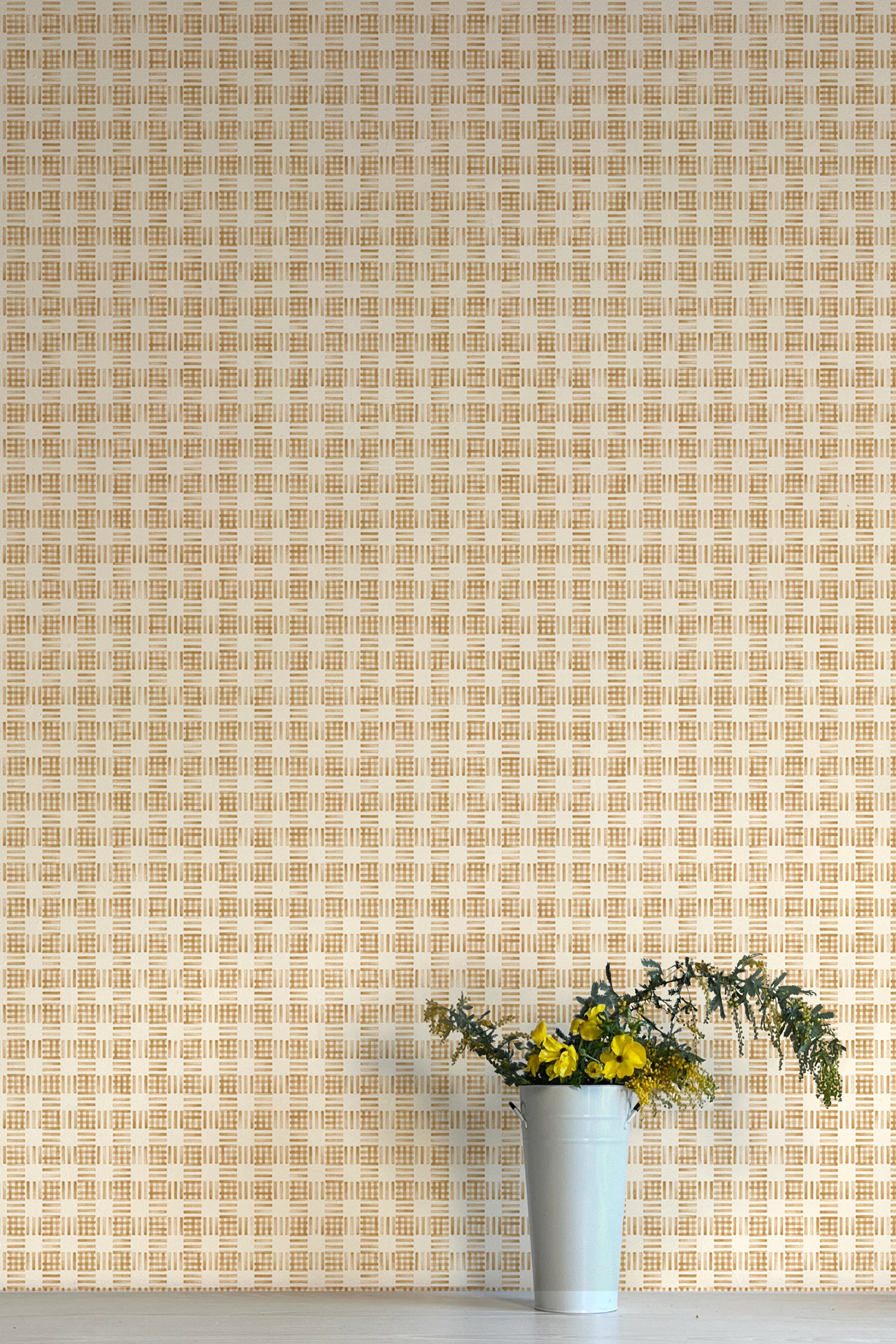 A vase of flowers stands in front of a wall papered in a dense plaid pattern in shades of orange and tan.