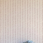 A vase of flowers stands in front of a wall covered in a repeating striped circular print in purple on a cream field.