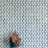 A vase of flowers stands in front of a wall papered in a playful curvy stripe print in navy on a light blue field.