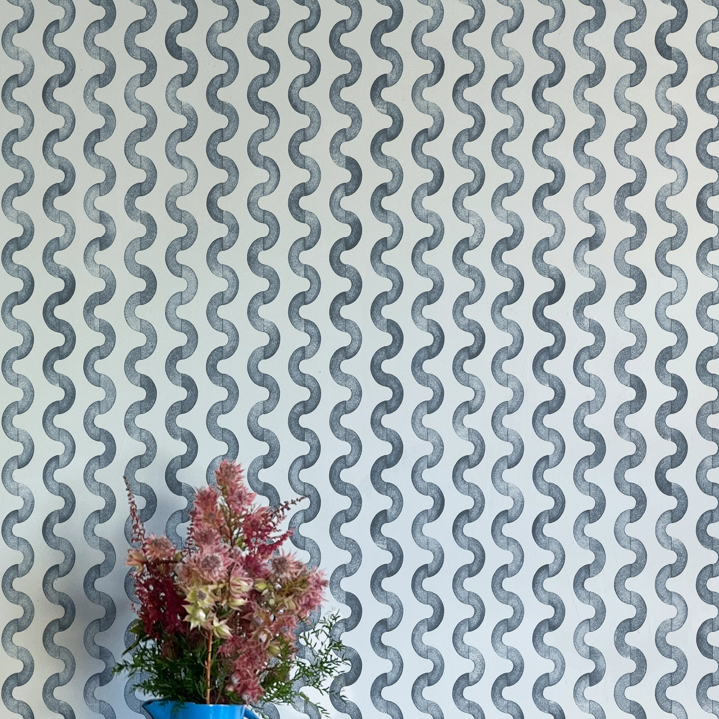 A vase of flowers stands in front of a wall papered in a playful curvy stripe print in navy on a light blue field.