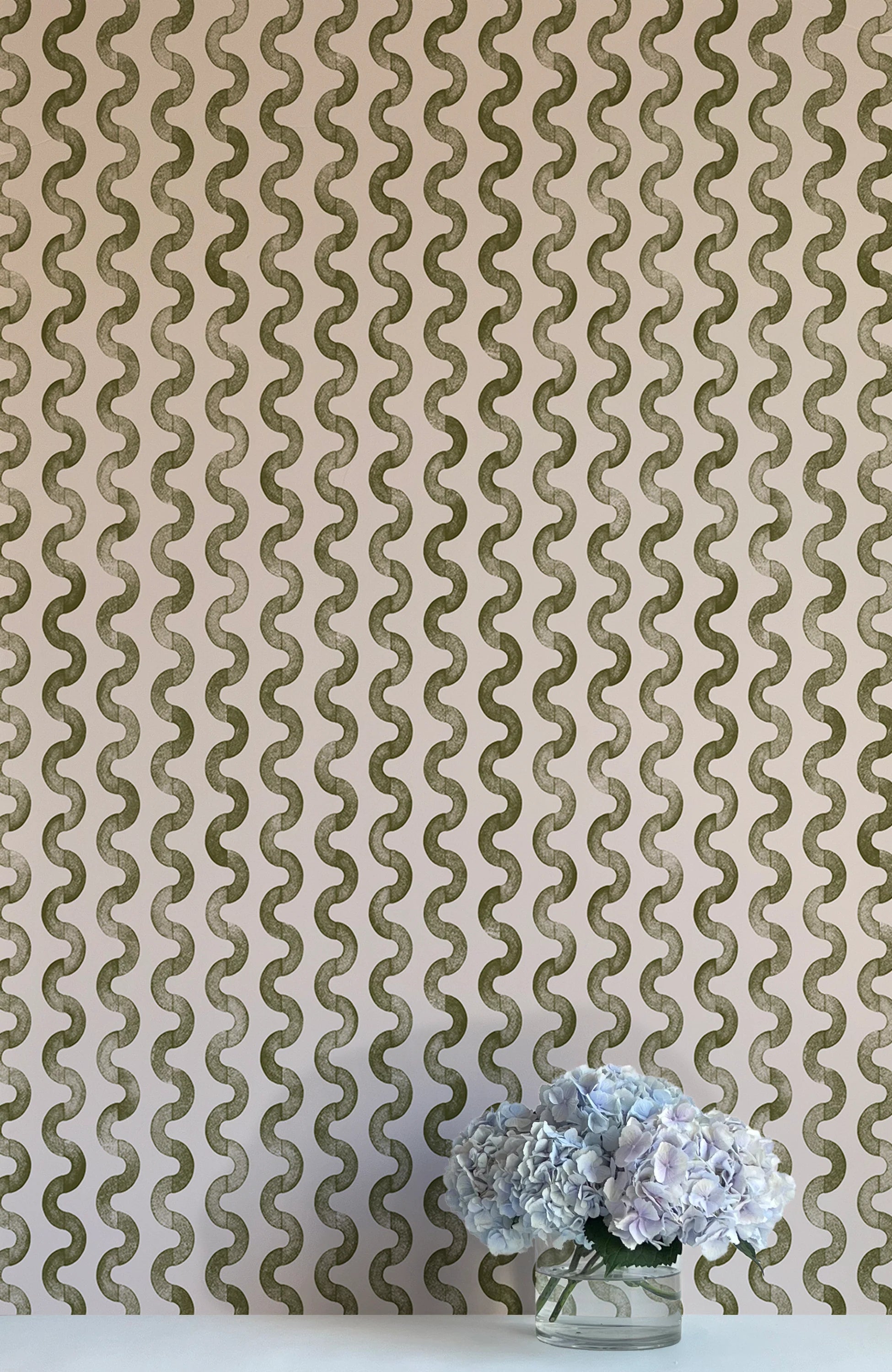 A vase of flowers stands in front of a wall papered in a playful curvy stripe print in green on a light pink field.