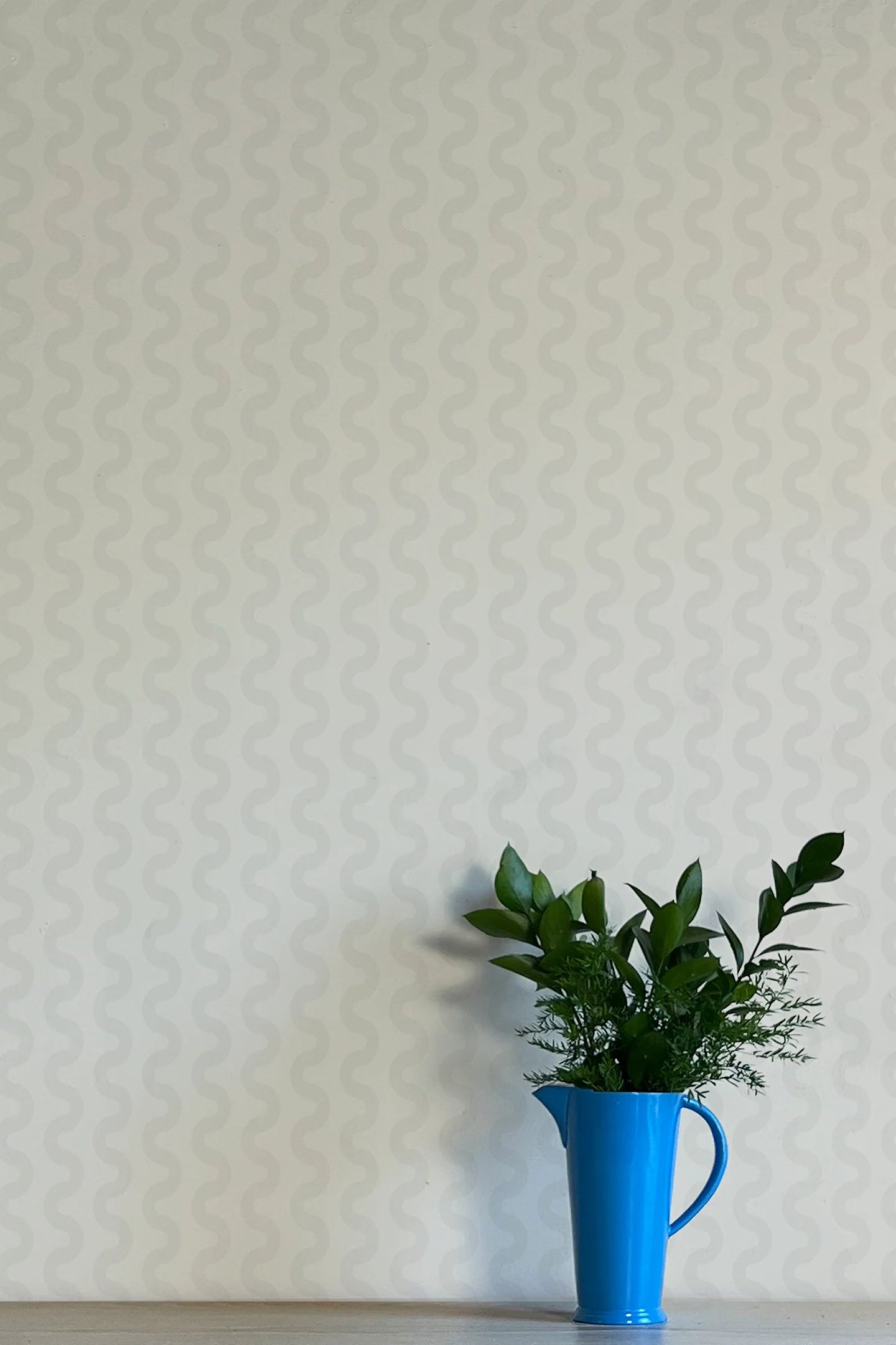 A vase of flowers stands in front of a wall papered in a playful curvy stripe print in gray on a light gray field.