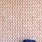 A vase of flowers stands in front of a wall papered in a playful curvy stripe print in red on a cream field.