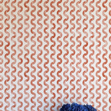 A vase of flowers stands in front of a wall papered in a playful curvy stripe print in red on a cream field.