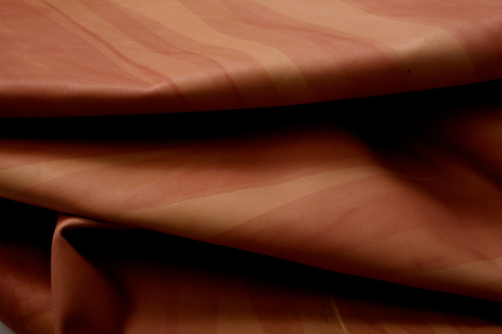 Draped upholstery leather in orange with an abstract stripe overlay in shades of orange and brown.