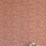 A vase of flowers stands in front of a wall covered in a textural grid print in shades of red and cream.