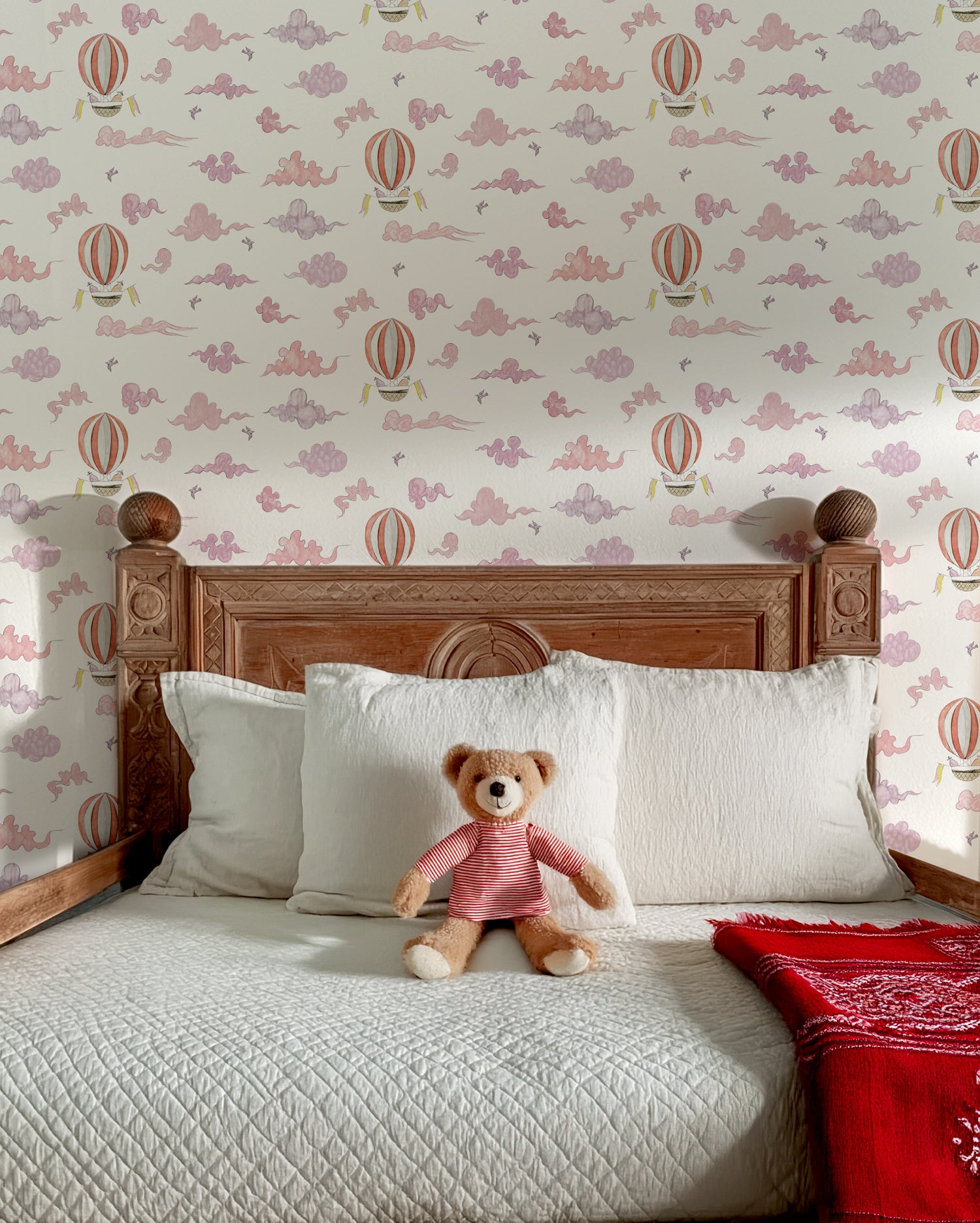 Bedroom with wooden headboard, white pillows, teddy bear, and hot air balloon wallpaper.