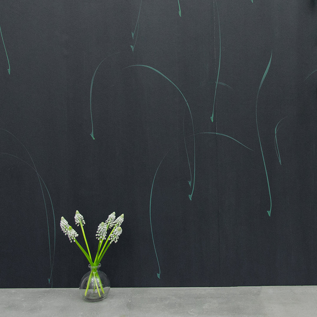 A vase of flowers stands in front of a wall papered in an elongated paint splatter pattern in turquoise on a navy field.