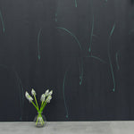 A vase of flowers stands in front of a wall papered in an elongated paint splatter pattern in turquoise on a navy field.