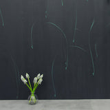 A vase of flowers stands in front of a wall papered in an elongated paint splatter pattern in turquoise on a navy field.