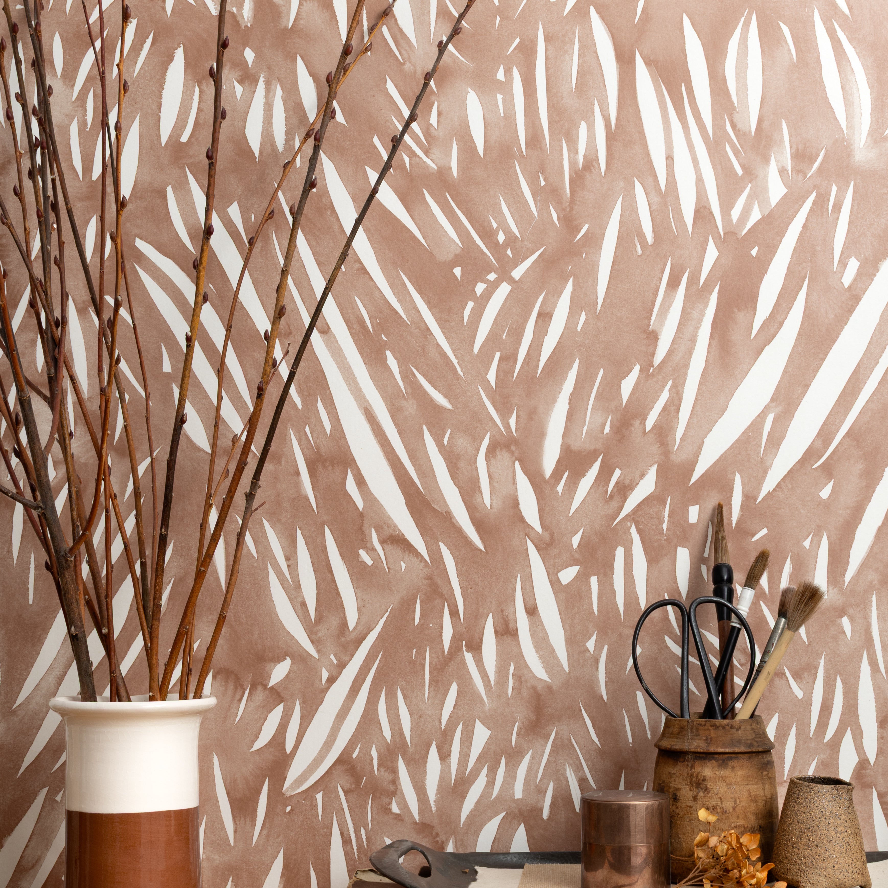 Mantle vignette with ceramic vases, branches and tailoring tools against wallpaper abstract leaf pattern in white on a terracotta watercolor field.