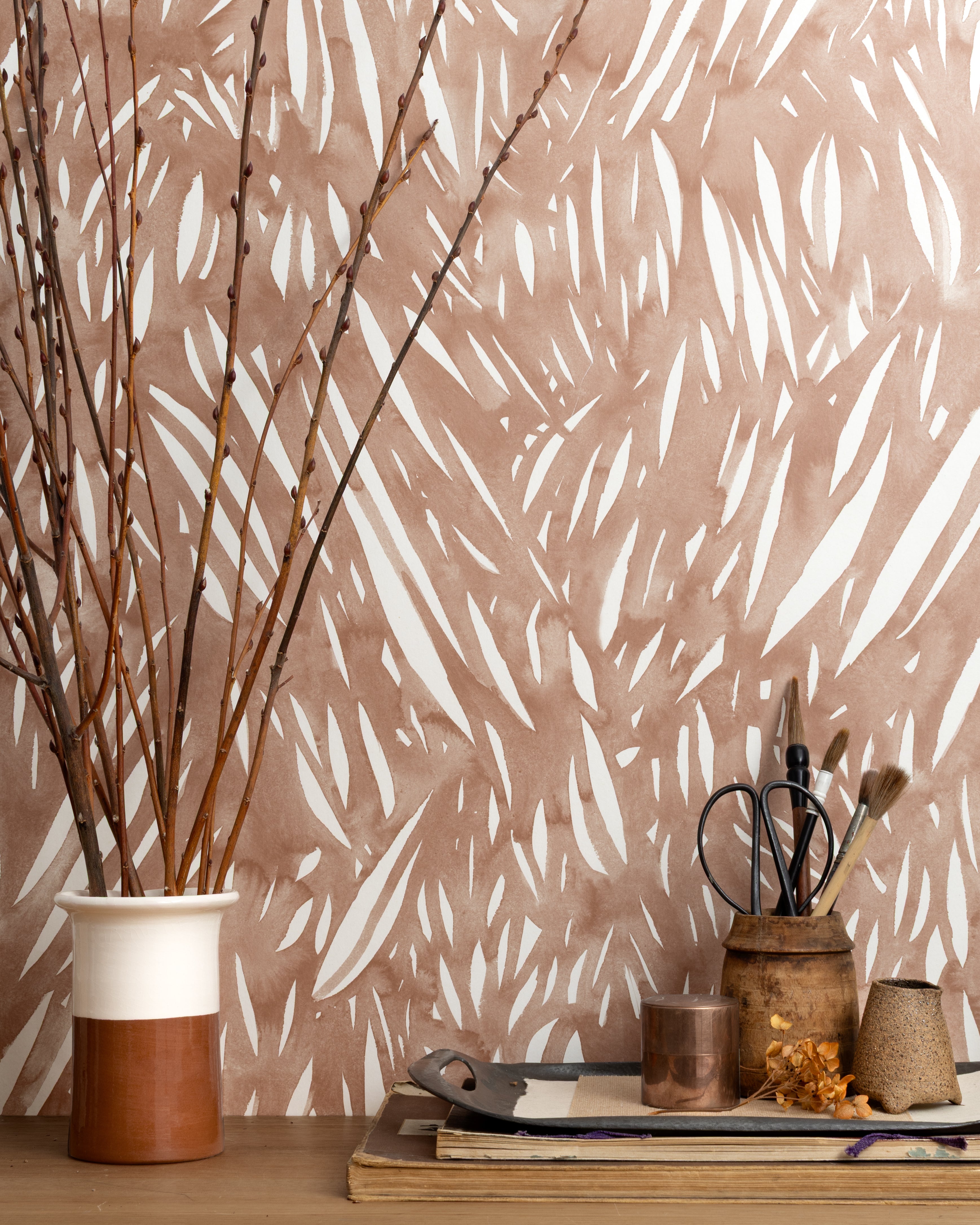 Mantle vignette with ceramic vases, branches and tailoring tools against wallpaper abstract leaf pattern in white on a terracotta watercolor field.