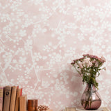 Mantle vignette with vase and flowers and antique books in front of a wallpapered in painterly branch print in white on a pale pink field.