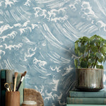 Mantle vignette with antique books, potted plant and pencil jar against wallpaper  in a playful wave print in white on a chambray blue field.