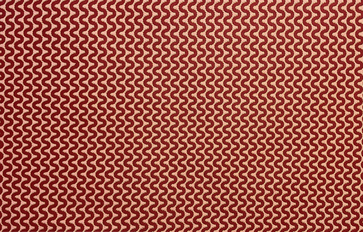 Detail of fabric in a playful curving stripe in red on an orange field.