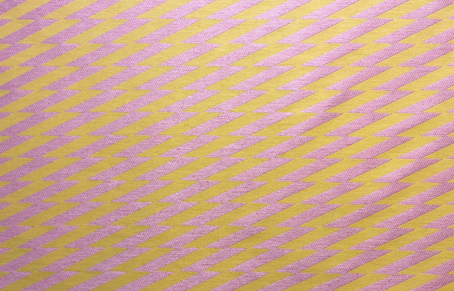 Detail of fabric in a zigzag stripe print in pink on a mustard field.
