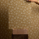 Hand holding a sheet of floral-patterned wallpaper against a matching wall.