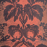 Detail of wallpaper in a repeating floral damask pattern in brown on a red field.