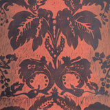 Detail of wallpaper in a repeating floral damask pattern in brown on a red field.