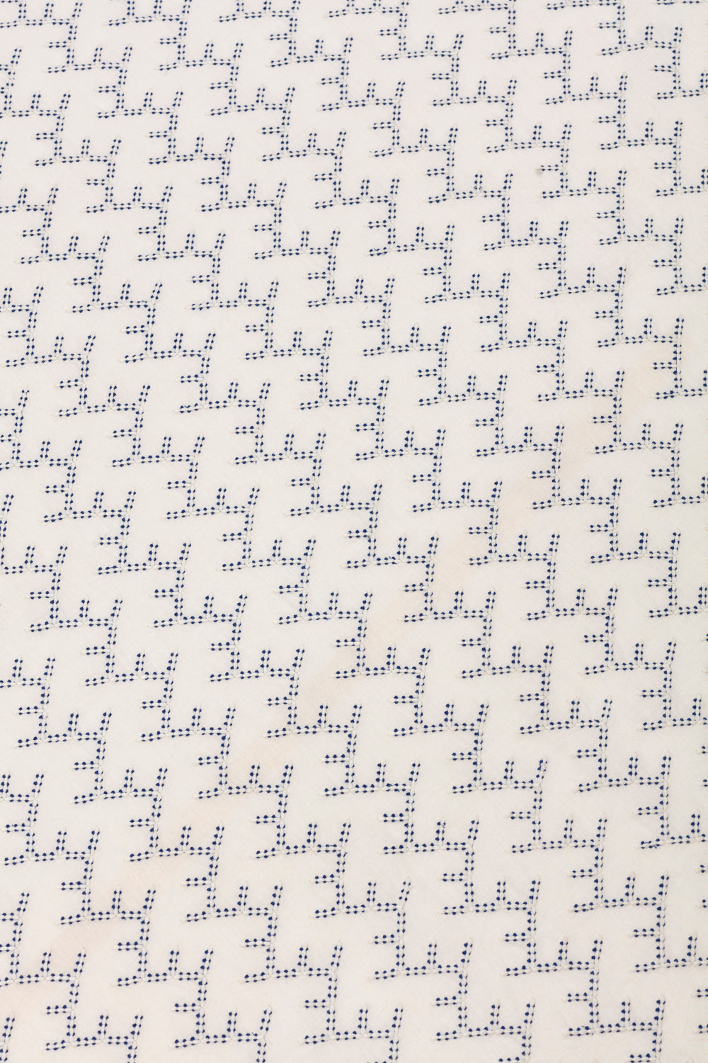 Detail of embroidered fabric in a linear geometric print in white and navy on a cream field.