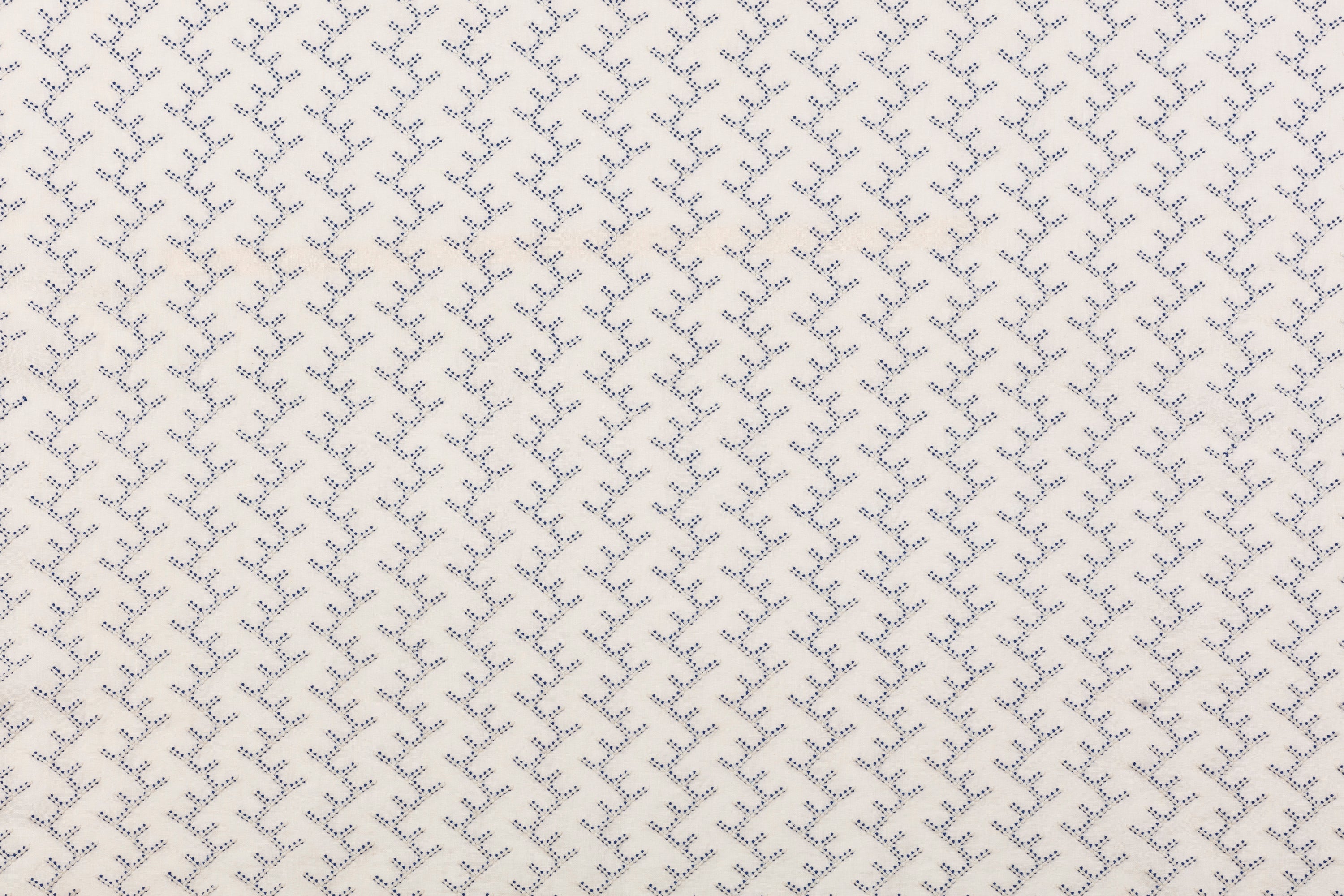 Panel of embroidered fabric in a linear geometric print in white and navy on a cream field.