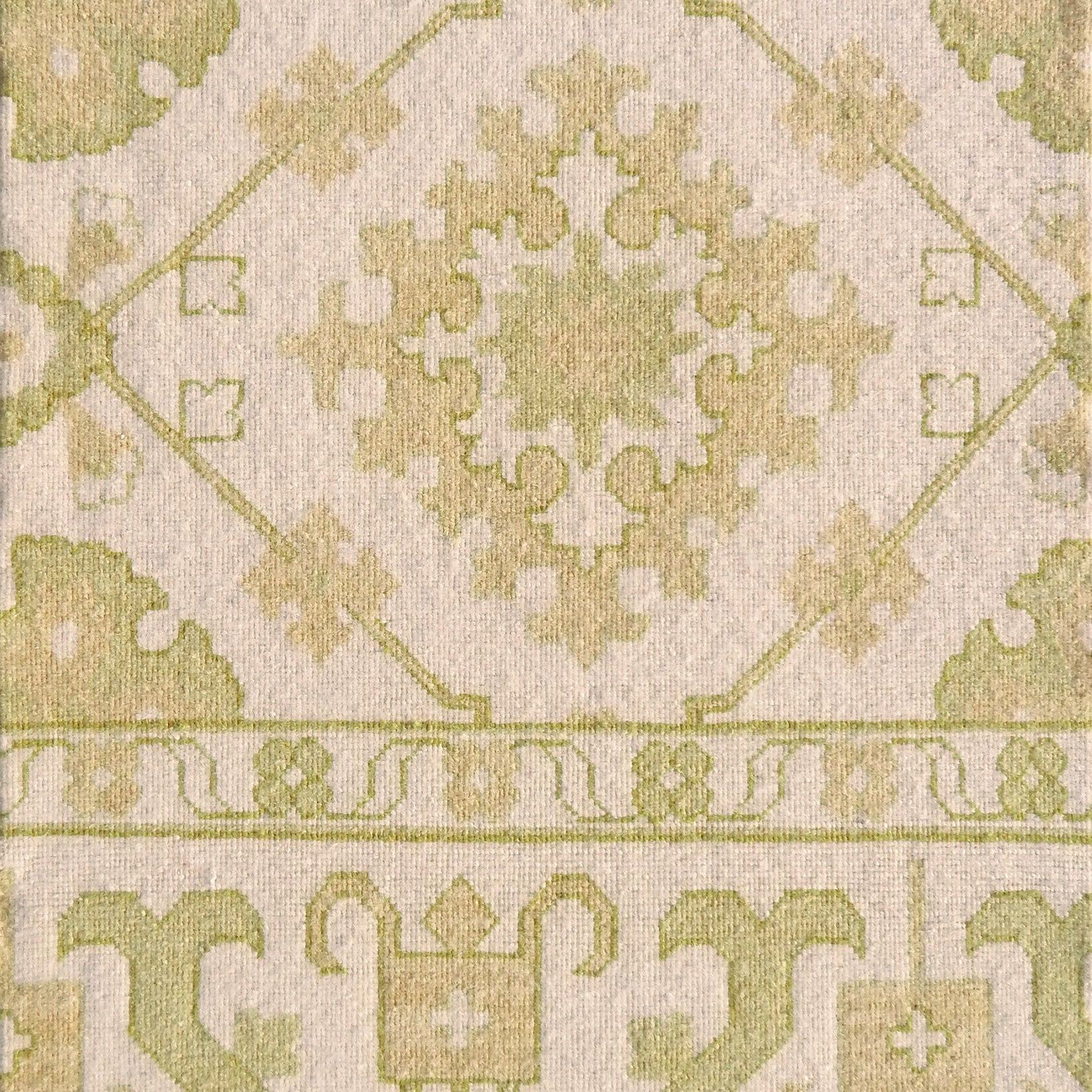 Detail of a handmade rug with with ornate green and cream design.
