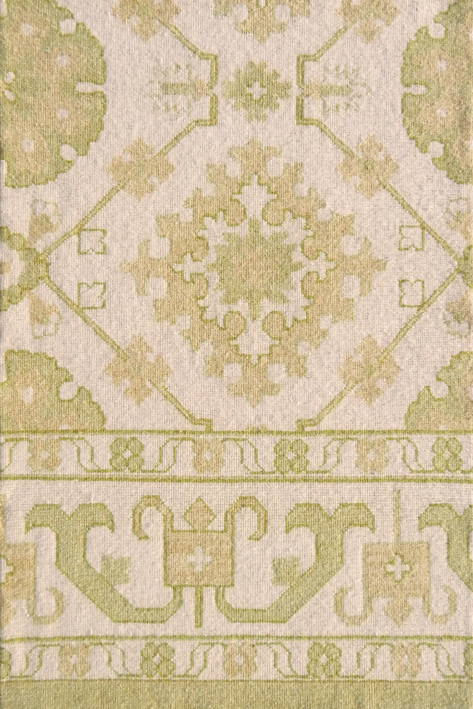 Detail of a handmade rug with with ornate green and cream design.