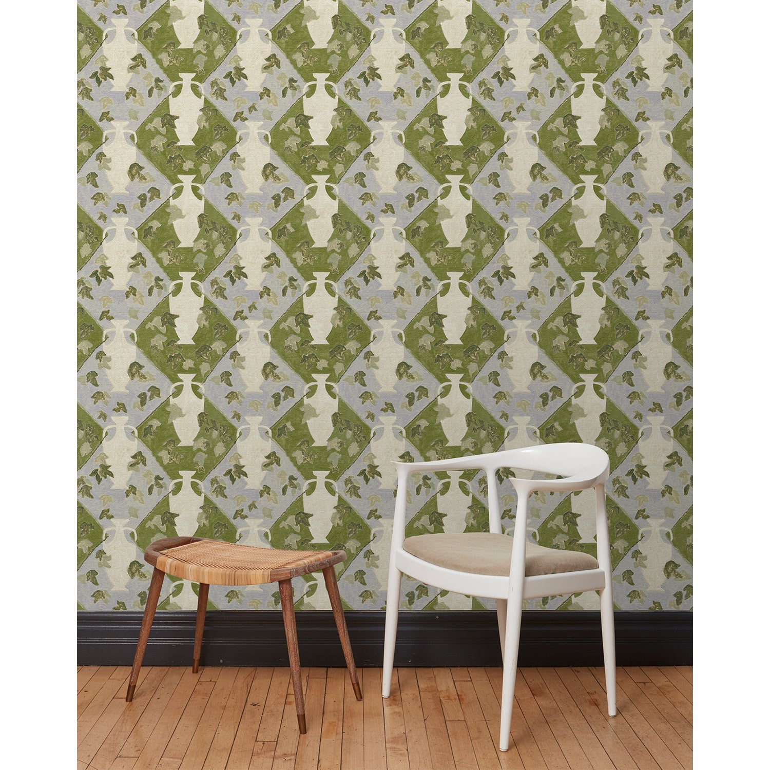 Chair and stool in front of a wall papered in a large, painterly vase and leaf print over a repeating diamond background in shades of green and blue.