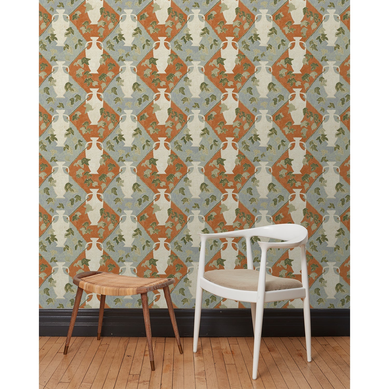 Chair and stool in front of a wall papered in a large, painterly vase and leaf print over a repeating diamond background in shades of blue and rust.