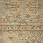A close-up of a vintage-style area rug with a distressed, low-pile texture. The design features muted beige, gray, and brown tones with traditional floral and geometric motifs.