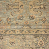 A close-up of a vintage-style area rug with a distressed, low-pile texture. The design features muted beige, gray, and brown tones with traditional floral and geometric motifs.