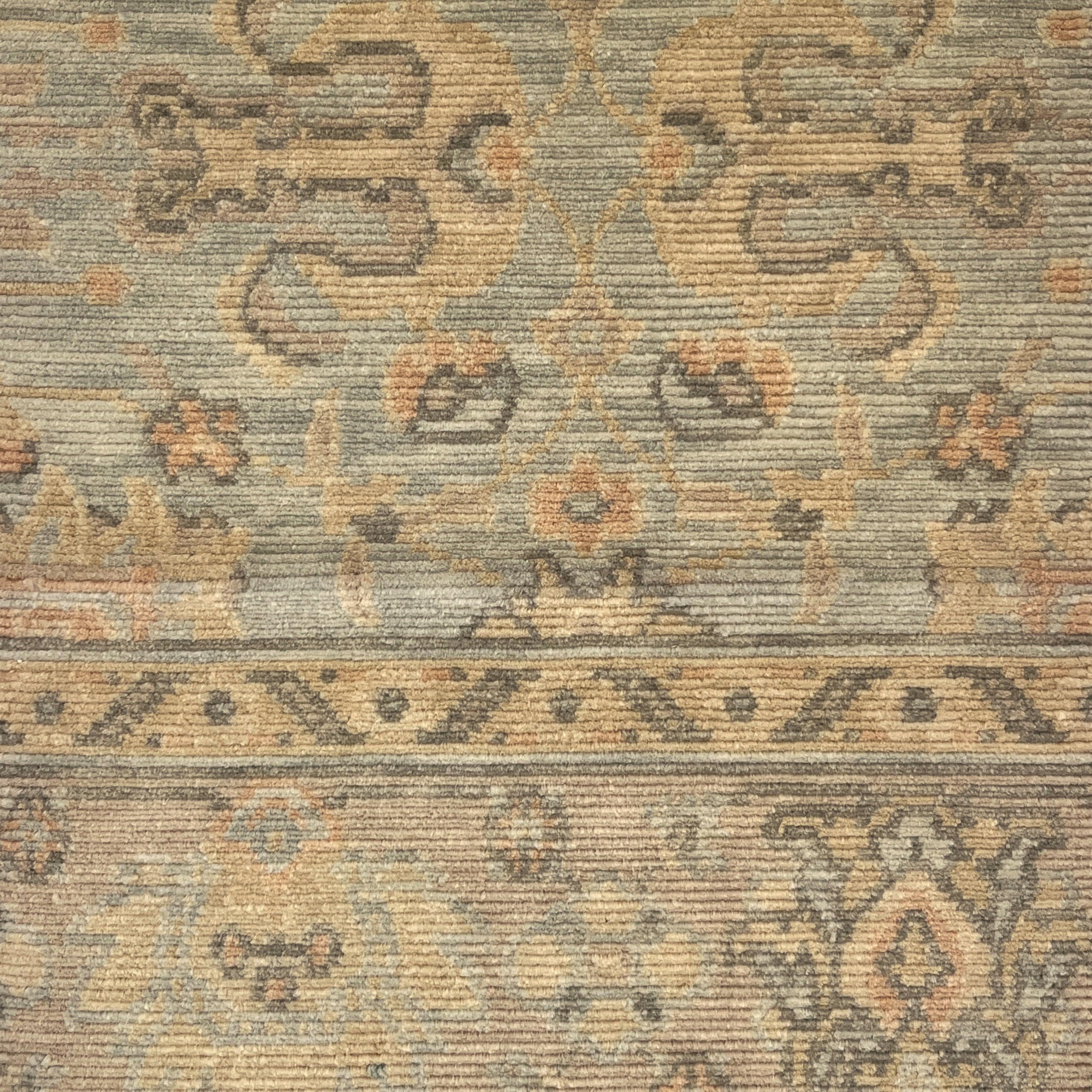 A close-up of a vintage-style area rug with a distressed, low-pile texture. The design features muted beige, gray, and brown tones with traditional floral and geometric motifs.