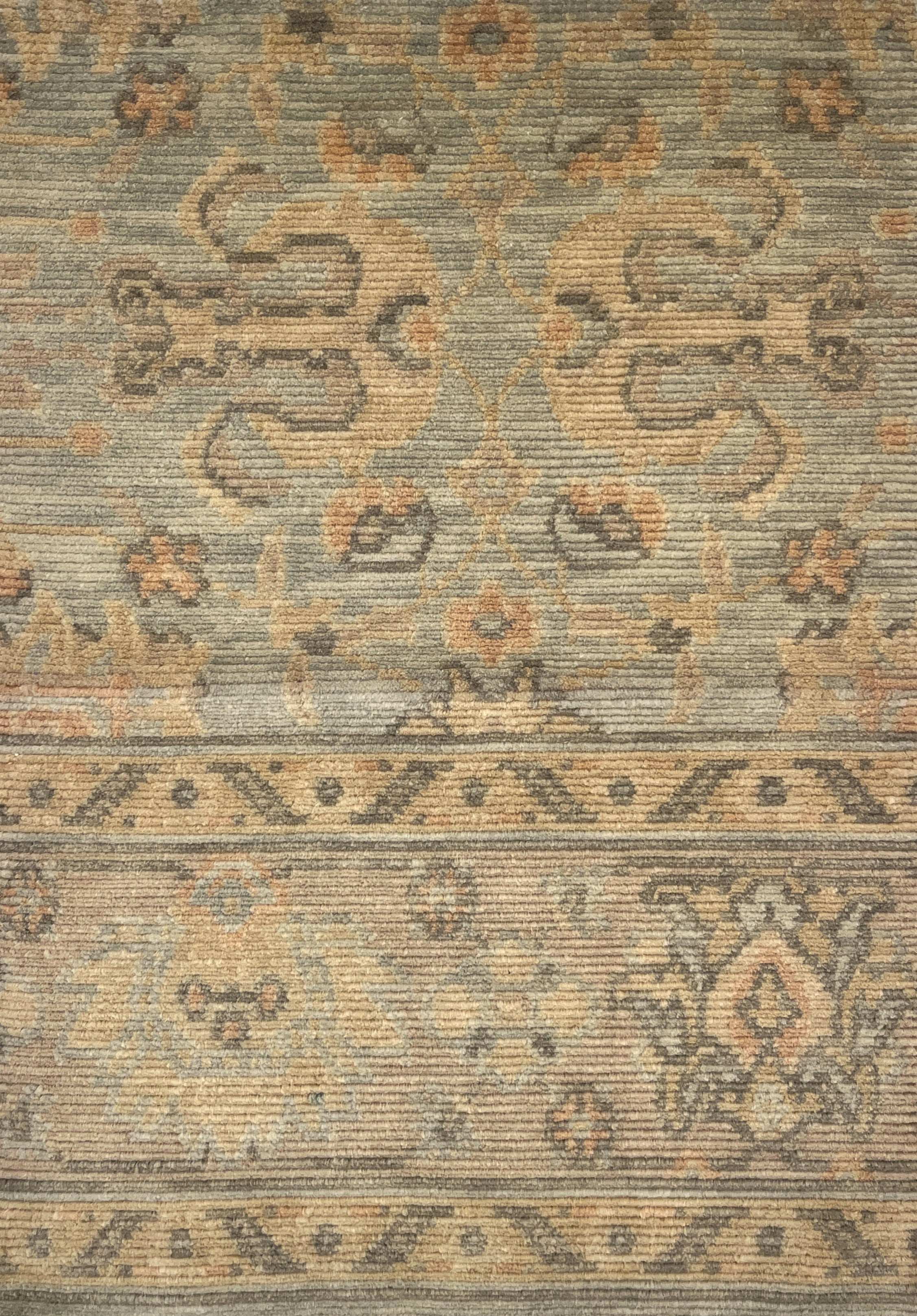 A close-up of a vintage-style area rug with a distressed, low-pile texture. The design features muted beige, gray, and brown tones with traditional floral and geometric motifs.