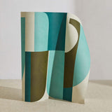 A curved partition stands on the ground, covered in a curvilinear geometric grid print in shades of turquoise, green and cream.