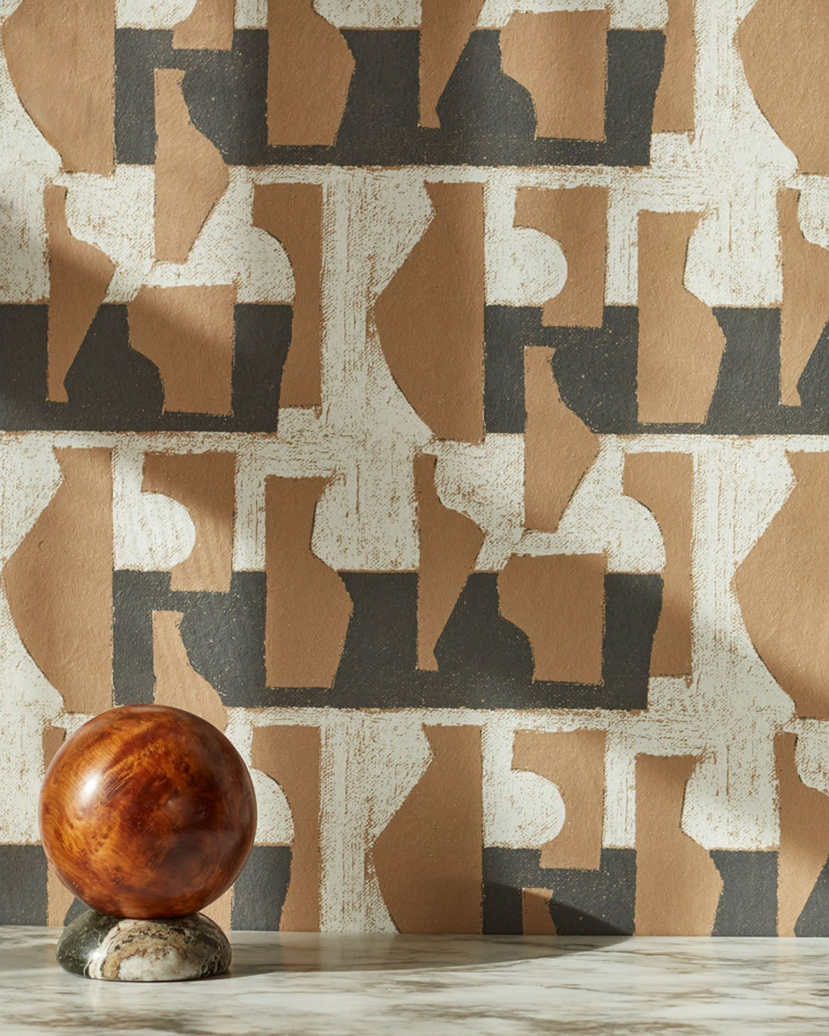 A sphere with marble base in front of a wall with a pattern of brown geometric vessel shapes over a white background with charcoal grey horizontal stripes.